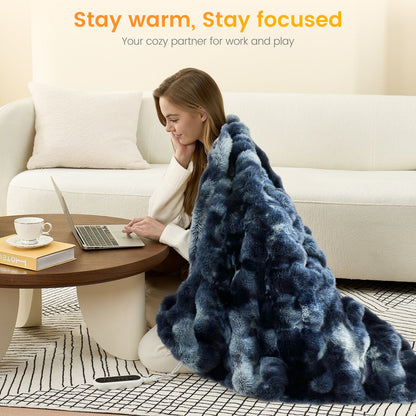 Woman using a laptop on a coffee table with a tie-dye blue faux fur heated electric throw blanket draped over her, sitting on the floor in a cozy living room.   #color_Tie-dye Blue