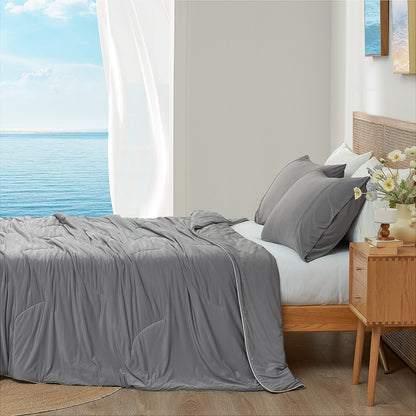 Dark grey cooling comforter on bed side view with sea, offering breathable bedding for a cozy sleep. #color_Dark Grey