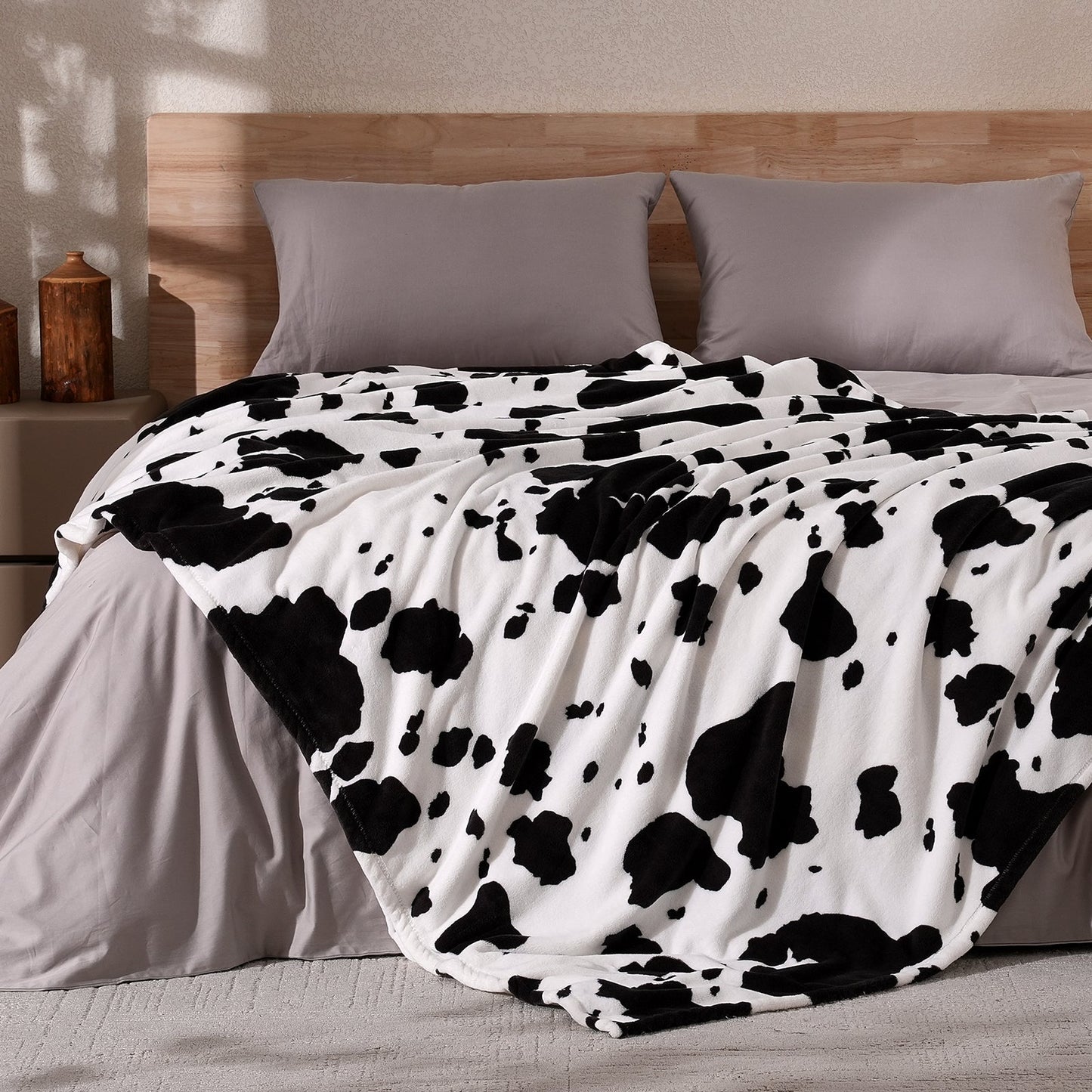 Cow print milkyplush throw blanket in Black White draped over a bed, creating a stylish atmosphere #color_Black White