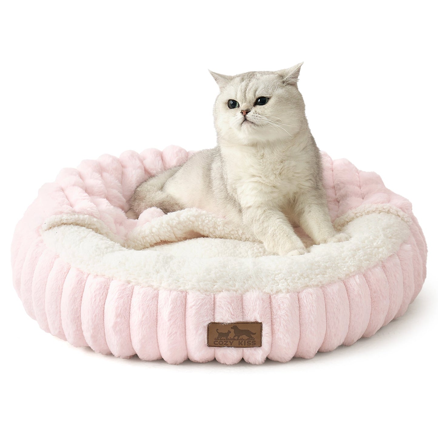 Cat lying on a fluffy pink faux fur pet bed with hooded blanket in a cozy room with wooden furniture and a rug.#color_Pink