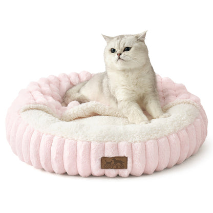 Cat lying on a fluffy pink faux fur pet bed with hooded blanket in a cozy room with wooden furniture and a rug.#color_Pink