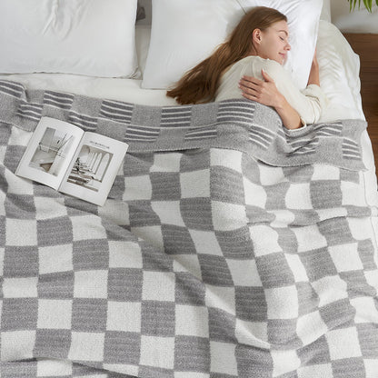 Woman relaxing in bed under a Reversible Heather Checkered Feather Yarn Throw Blanket in Grey, offering warmth and comfort. #color_Grey