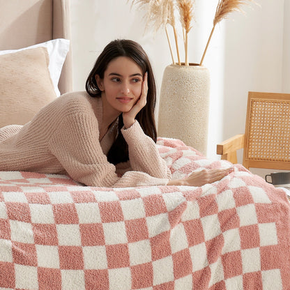 Woman lying on a bed with a Checkered Feather Yarn Knit Throw Blanket in Pink in a cozy living room setting. #color_Pink