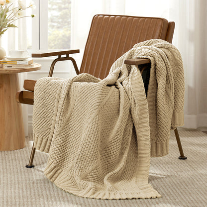 Ivory knitted blanket draped over a beige armchair in a room with a table and window. #color_Beige