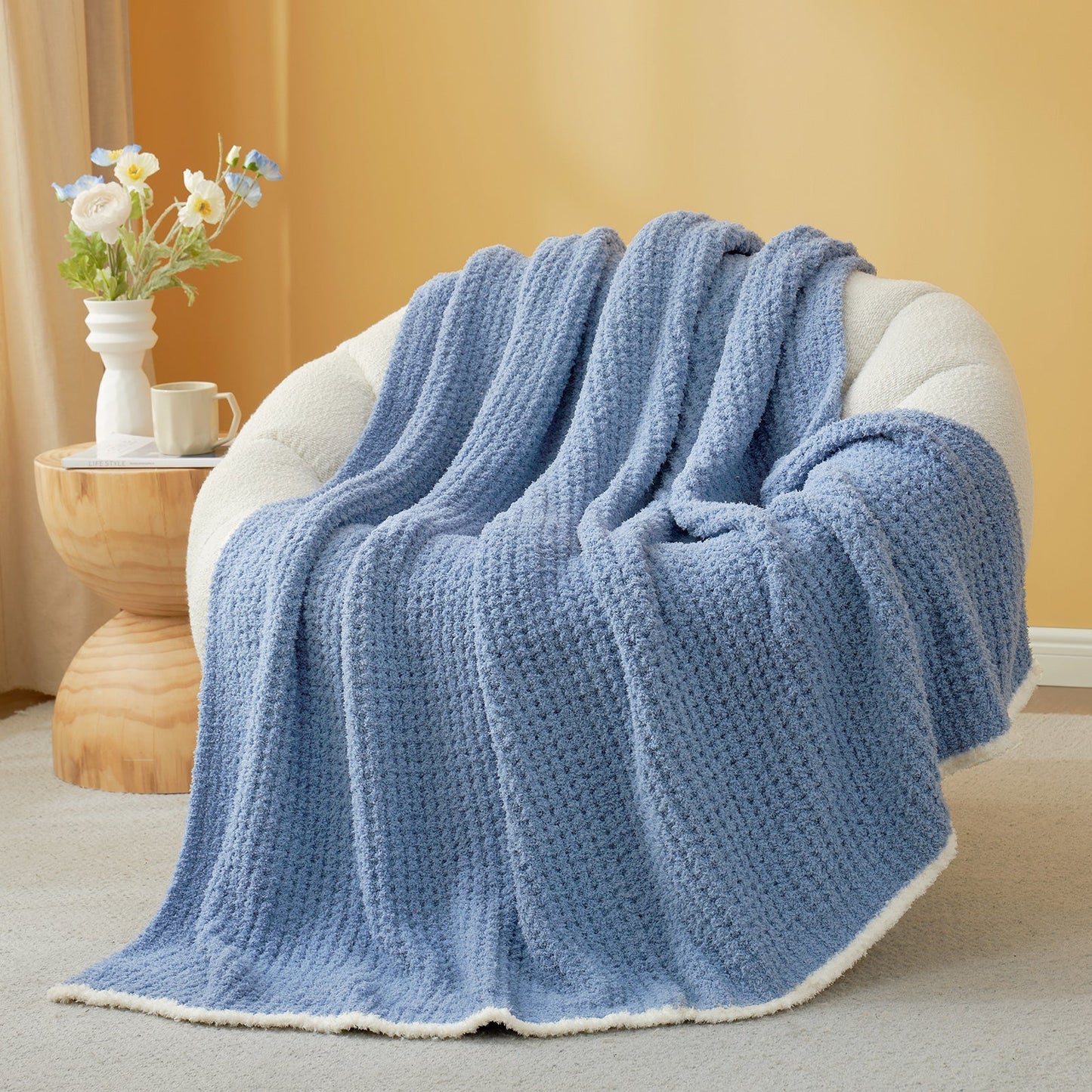 Denim Blue textured blanket draped over a chair with a side table and flowers in the background. #color_Denim Blue