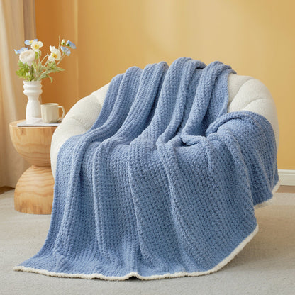 Denim Blue textured blanket draped over a chair with a side table and flowers in the background. #color_Denim Blue