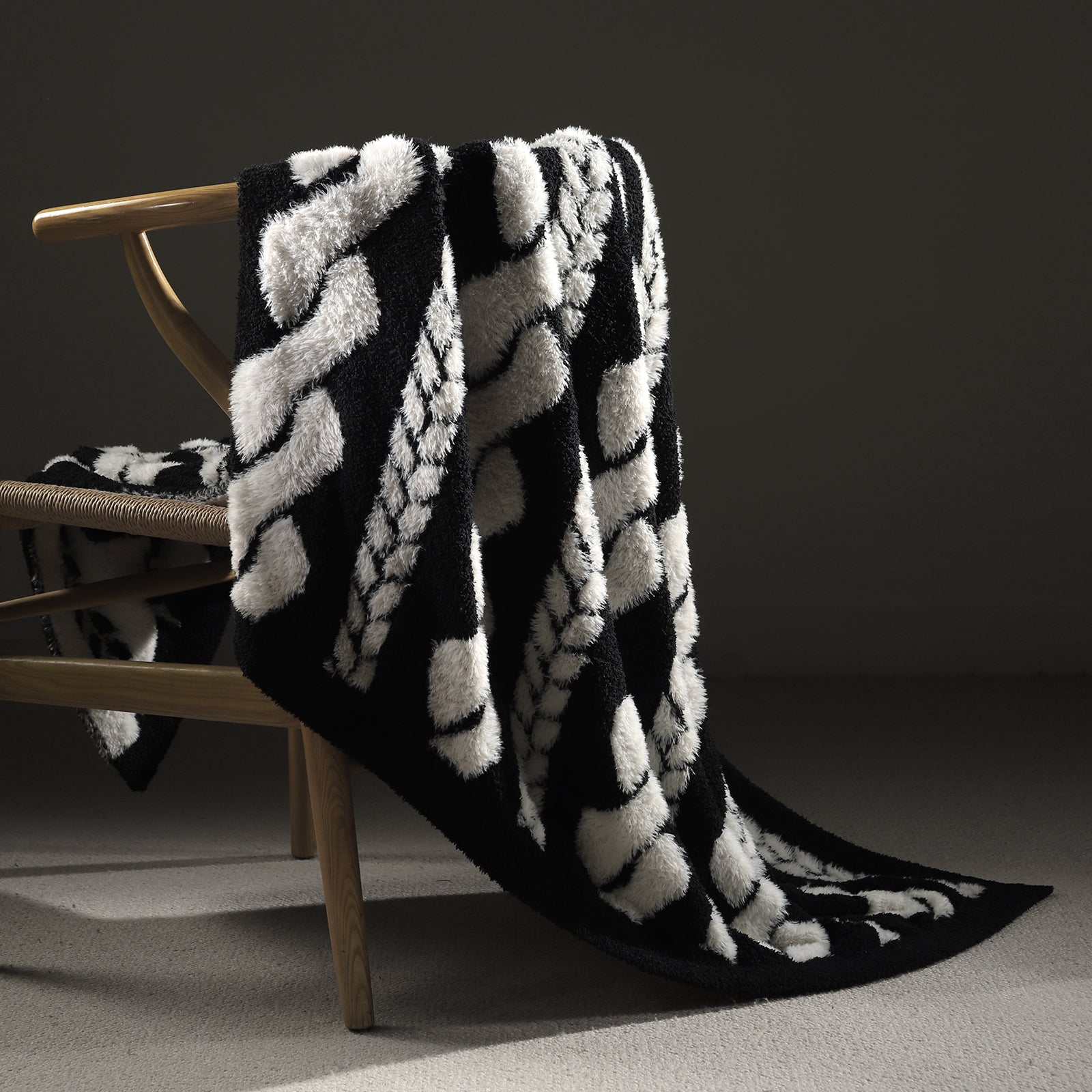 Faux Mink Cable Knit Throw Blanket in Black draped over a chair, showcasing plush texture and elegant cable knit design. #color_Black