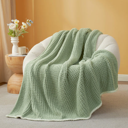 Sage Green textured blanket draped over a chair with a side table and flowers in the background. #color_Sage Green