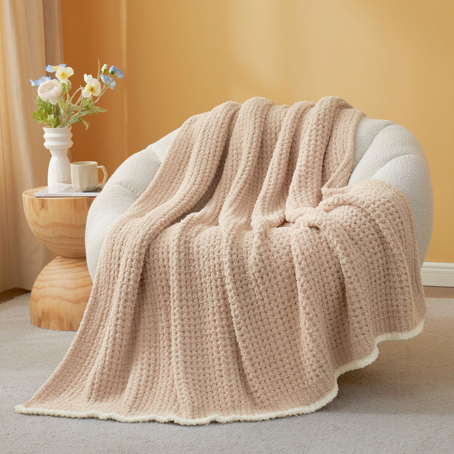 Beige textured blanket draped over a chair with a side table and flowers in the background. #color_Beige
