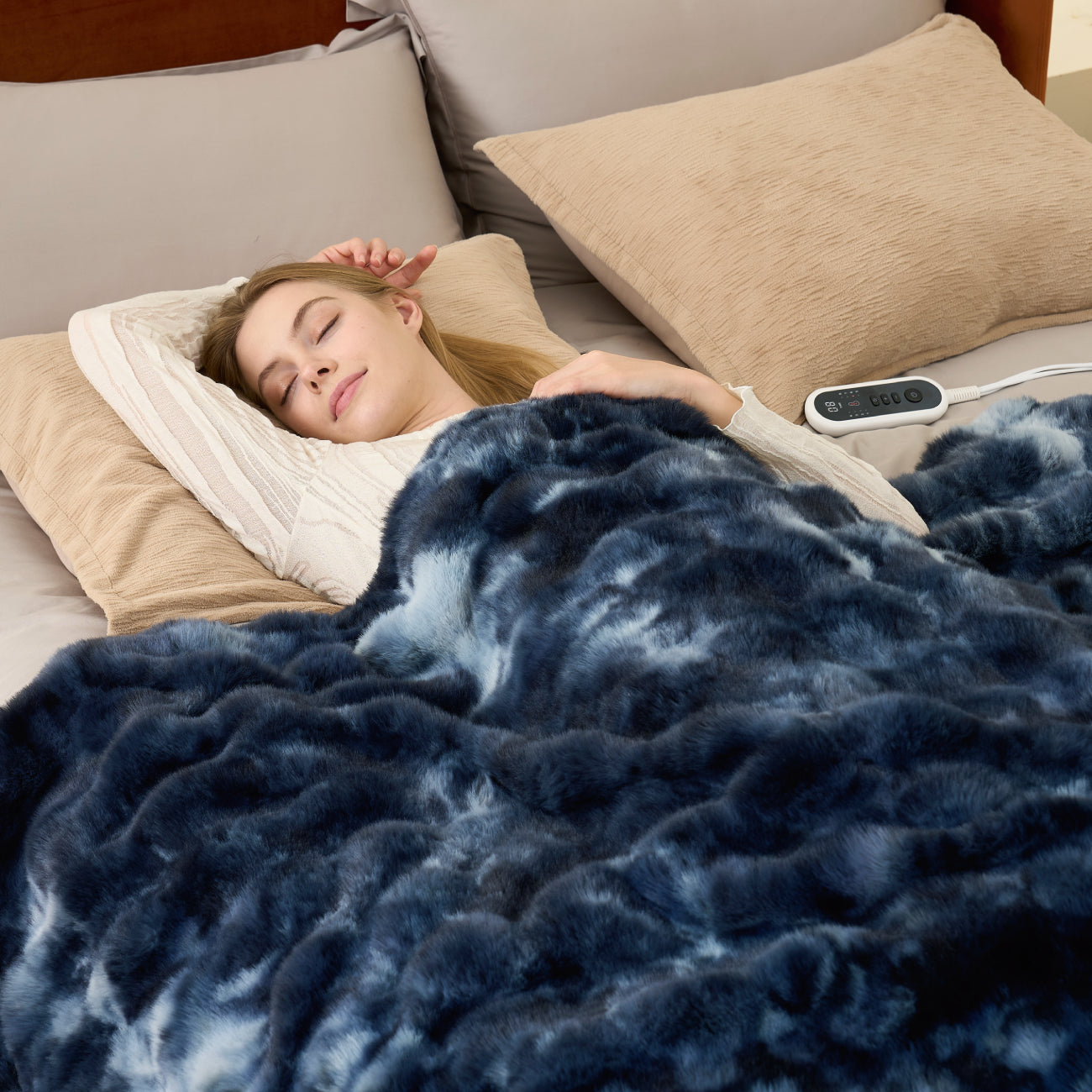 Woman sleeping under a tie-dye blue heated electric blanket with a remote control on a bed.  #color_Tie-dye Blue
