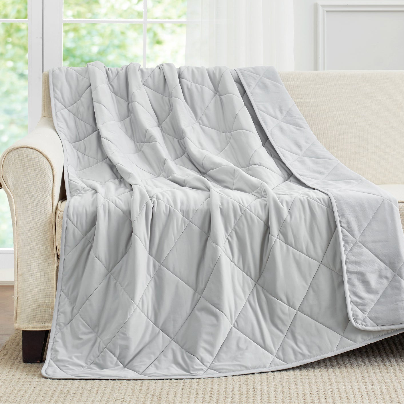 Cool grey cooling blanket draped over a beige sofa. #Color_Cool Grey