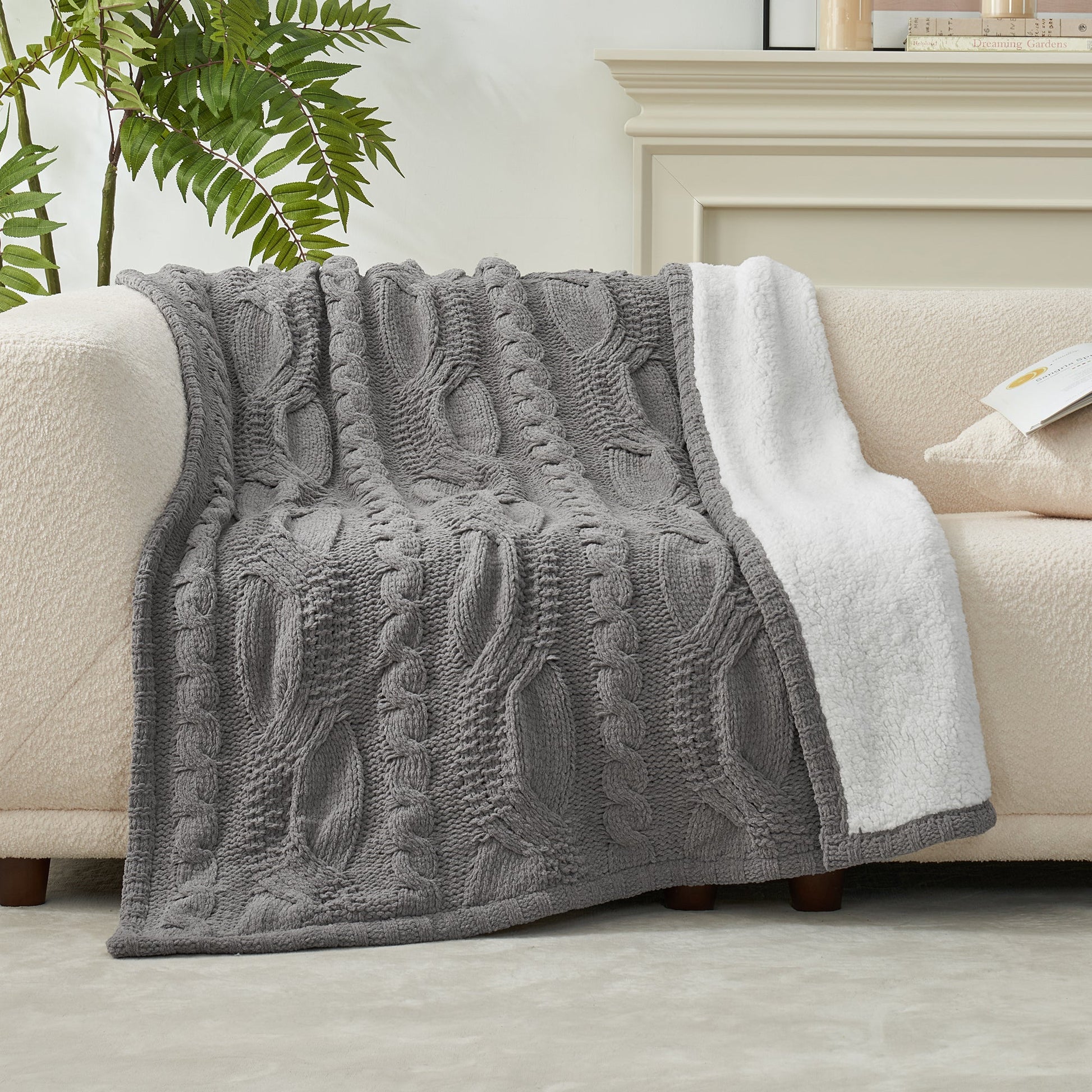 Reversible Cable Chenille Sherpa Knit Throw Blanket in Grey draped over a sofa, showcasing its textured cable knit design and soft sherpa lining. #color_Grey