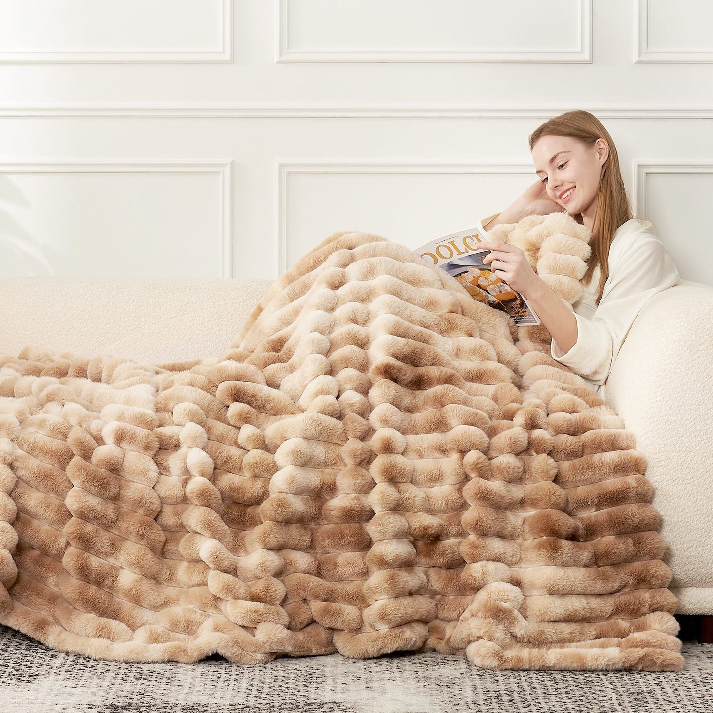 Woman reading on a couch wearing Striped faux fur blanket in tie-dye beige. #color_Tie-dye Beige