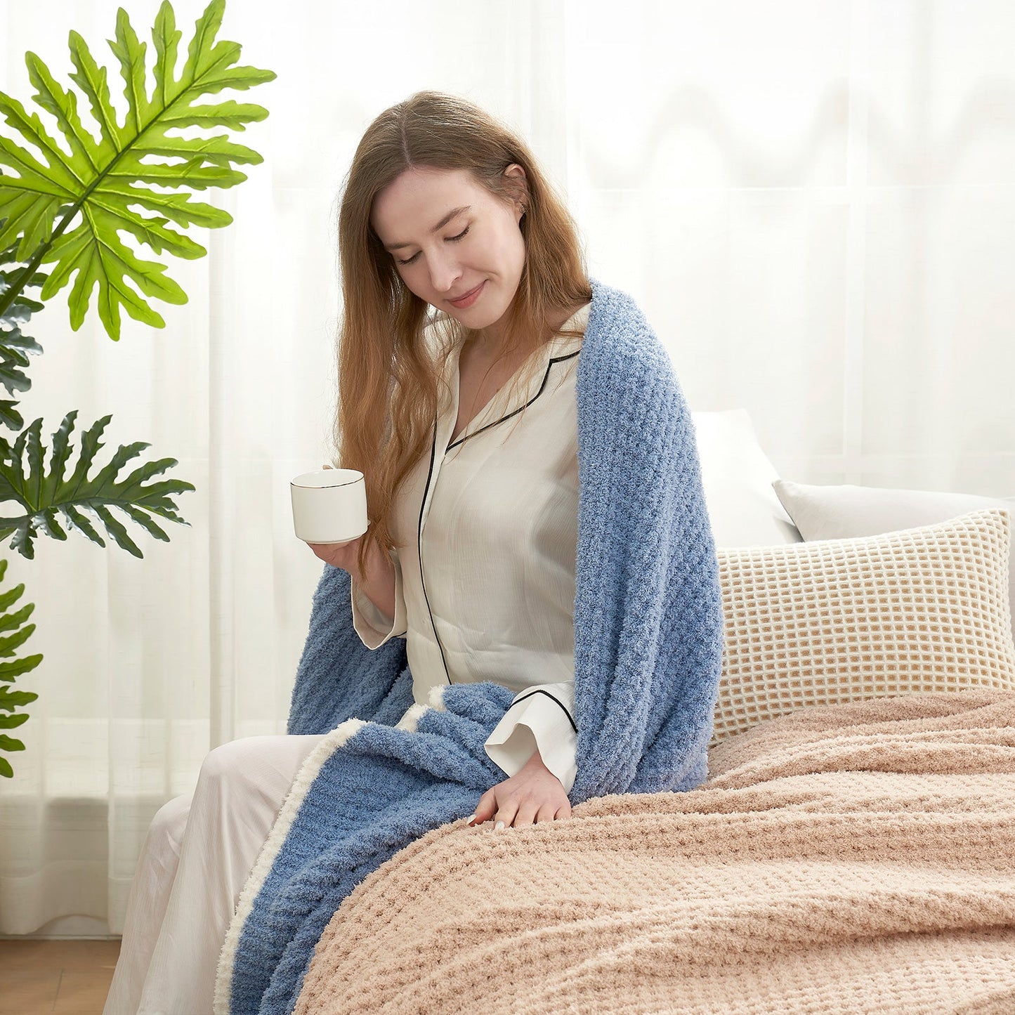 Woman enjoying a cup of coffee with a Soft Waffle Feather Yarn Throw Blanket in Denim Blue in a bright room setting. #color_Denim Blue