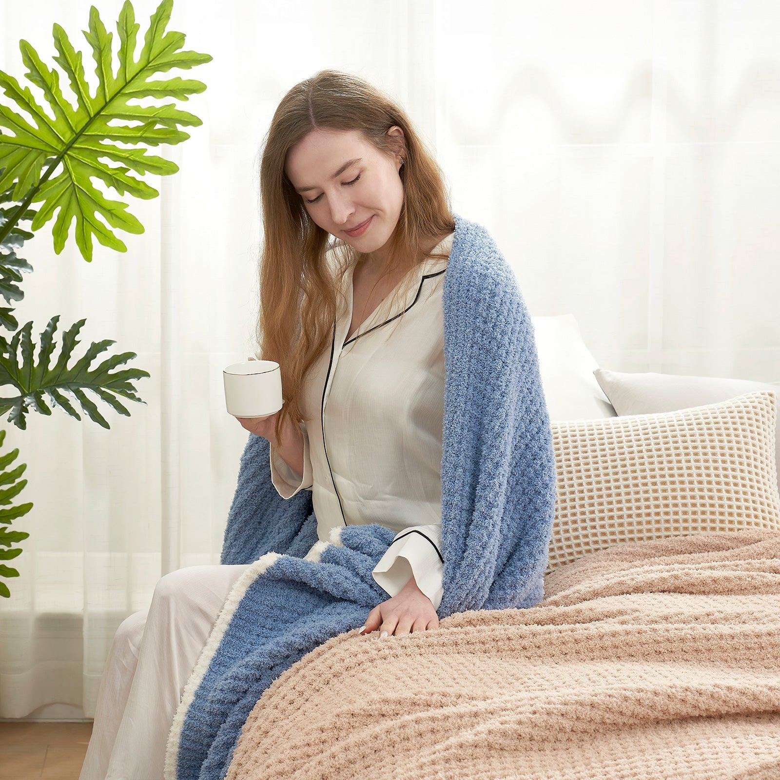 Woman enjoying a cup of coffee with a Soft Waffle Feather Yarn Throw Blanket in Denim Blue in a bright room setting. #color_Denim Blue