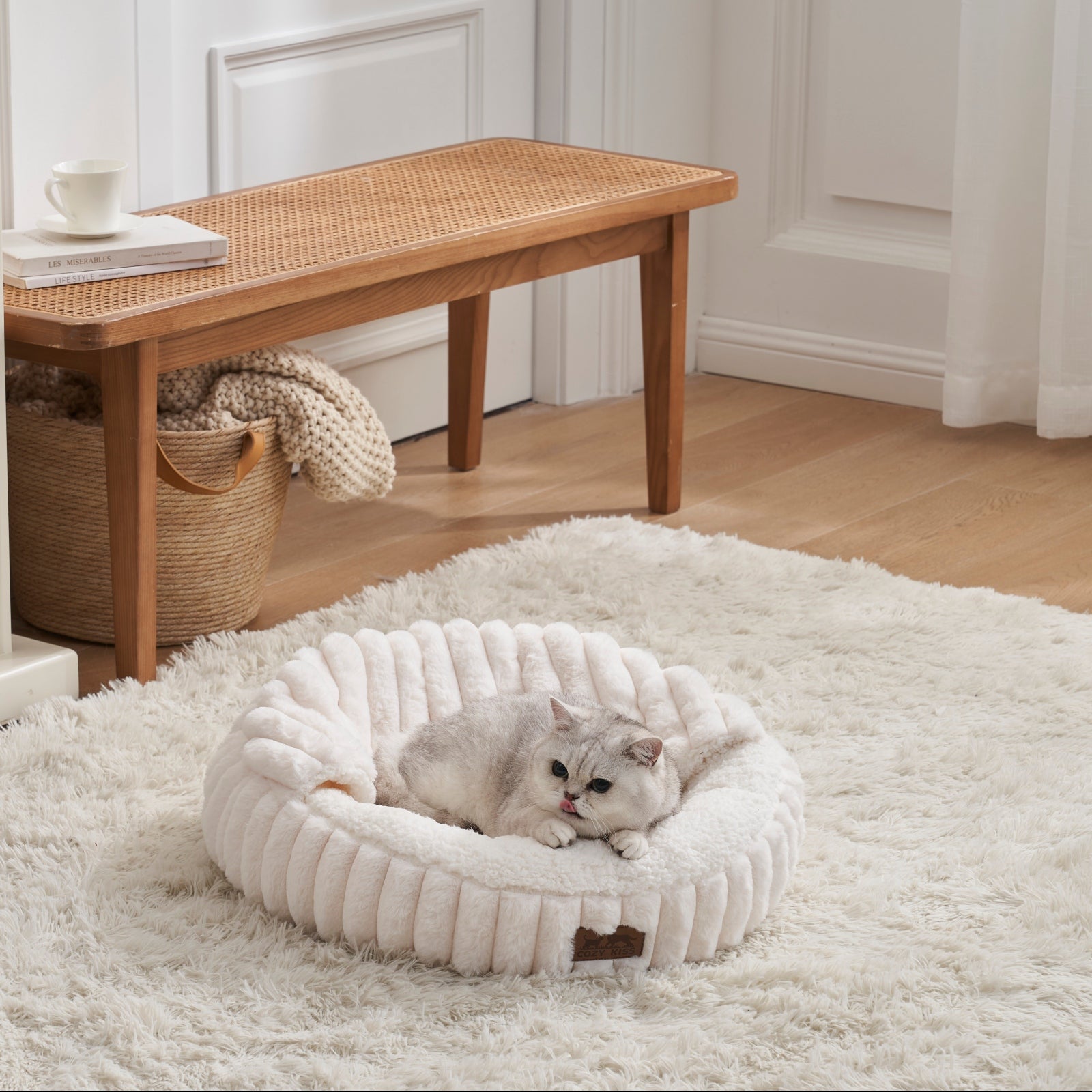 Cat lying on a fluffy white faux fur pet bed with hooded blanket in a cozy room with wooden furniture and a rug.#color_Cream Wite
