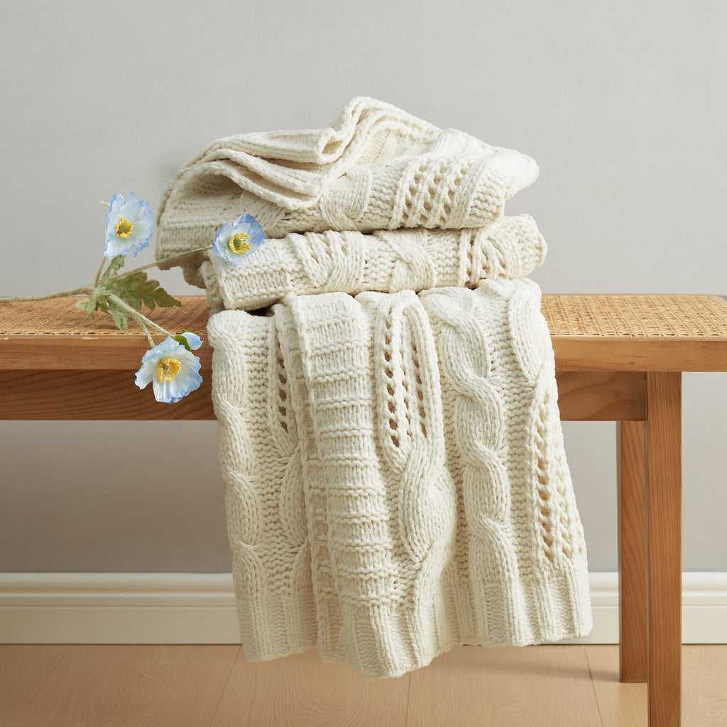 Chenille Cable Knit Throw Blanket in Ivory neatly folded on a table, showcasing detailed cable knit texture. #color_Ivory