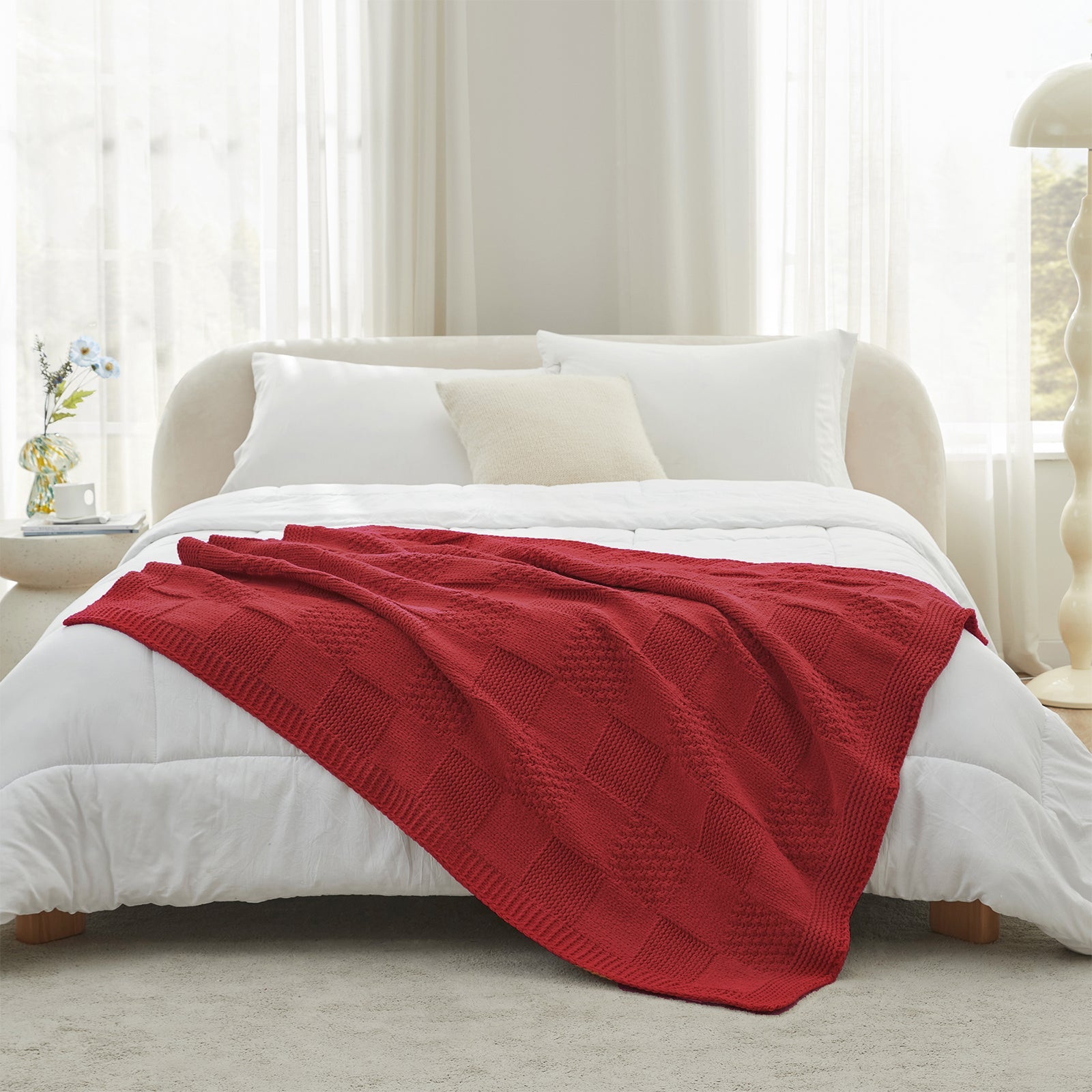 Red blanket on a bed in a bright bedroom with white bedding and curtains. #color_Red