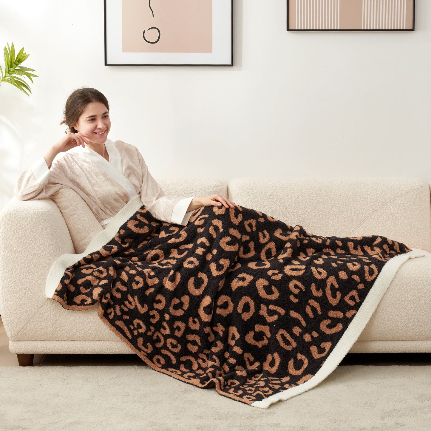 Woman relaxing on a sofa under a Reversible Leopard Feather Yarn Throw Blanket in Black, enjoying cozy comfort. #color_Black
